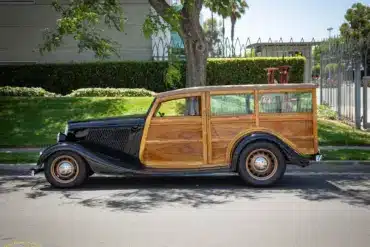 Seitliche Gesamtaufnahme eines 1934 Ford Station Wagon Replica Street Rod mit Karosserie aus Mango- und Koa-Holz, geparkt am Straßenrand bei Tageslicht
