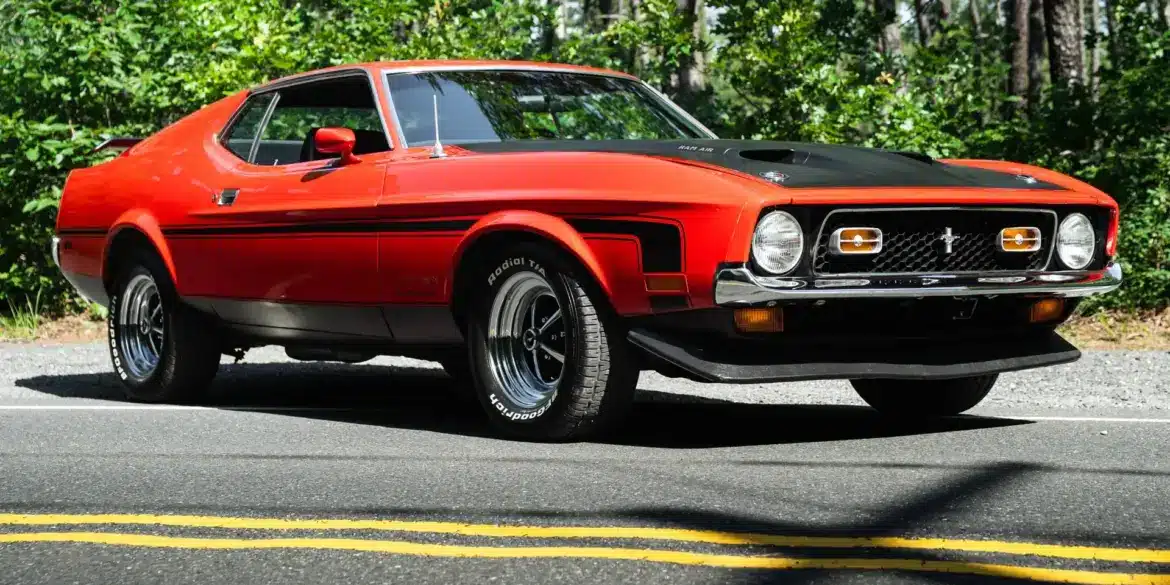 Roter Ford Mustang Mach 1 von 1971 geparkt auf Asphaltstraße vor Waldkulisse.