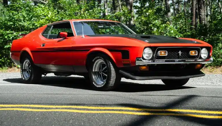 Roter Ford Mustang Mach 1 von 1971 geparkt auf Asphaltstraße vor Waldkulisse.