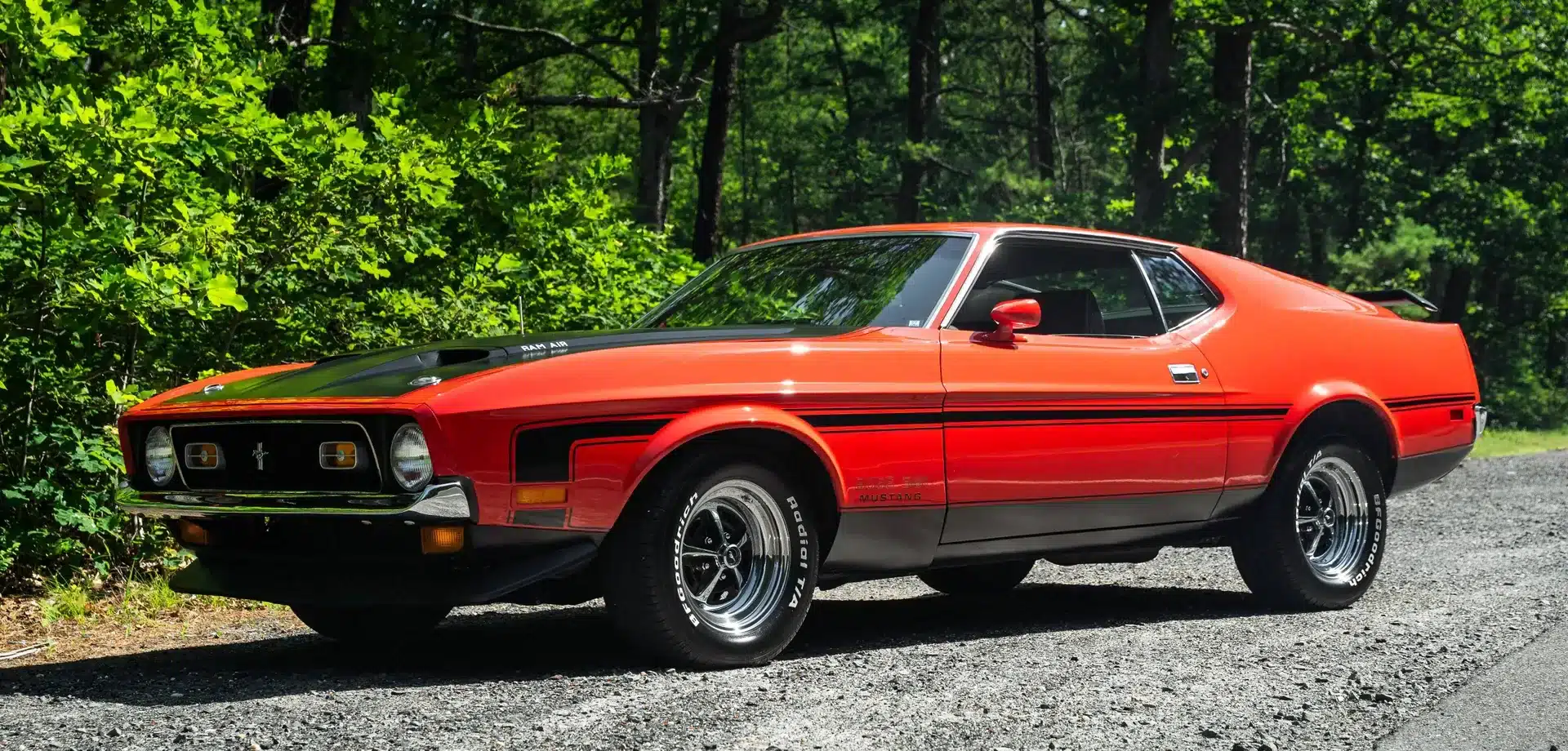 Ford Mustang Mach 1 1971, orange, auf einer Straße mit Bäumen im Hintergrund.