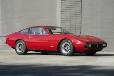 Roter Ferrari 365 GTC/4 aus dem Jahr 1972, geparkt vor einer Ziegelmauer.