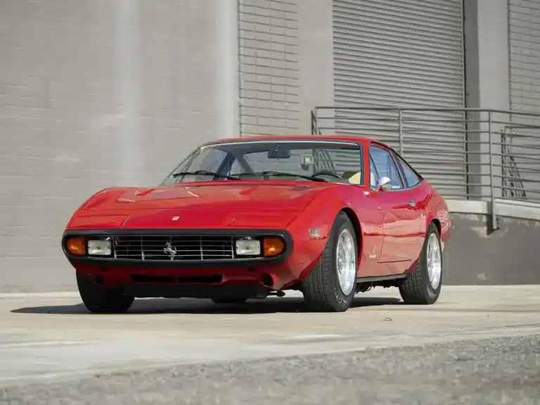 Ferrari 365 GTC/4, Baujahr 1972, in Rot, seitliche Frontansicht vor grauer Wand, klassisches Coupé-Design, fünfspeichige Leichtmetallfelgen.