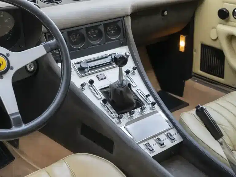 Innenraum und Cockpit mit Mittelkonsole eines Ferrari 365 GTC/4 von 1972, beige Lederausstattung, Schalthebel und Bedienelemente, klassisches Armaturenbrett.