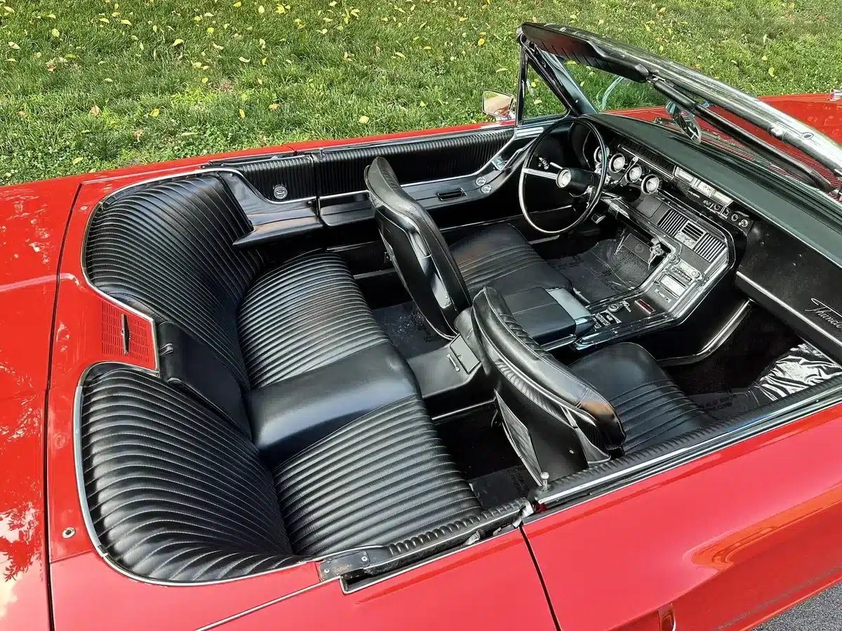 Offener Innenraum eines roten Ford Thunderbird Cabriolets von 1965 mit schwarzen Ledersitzen und klassischer Armaturentafel.