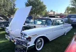 1957 Mercury Monterey Coupé in Classic White und Sunset Orchid mit geöffneter Motorhaube, vorgeführt auf einer Oldtimer-Ausstellung.