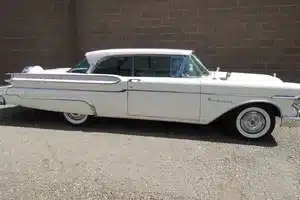 Seitenansicht eines Mercury Monterey Coupé Baujahr 1957 in weißer Lackierung vor einer Mauer.