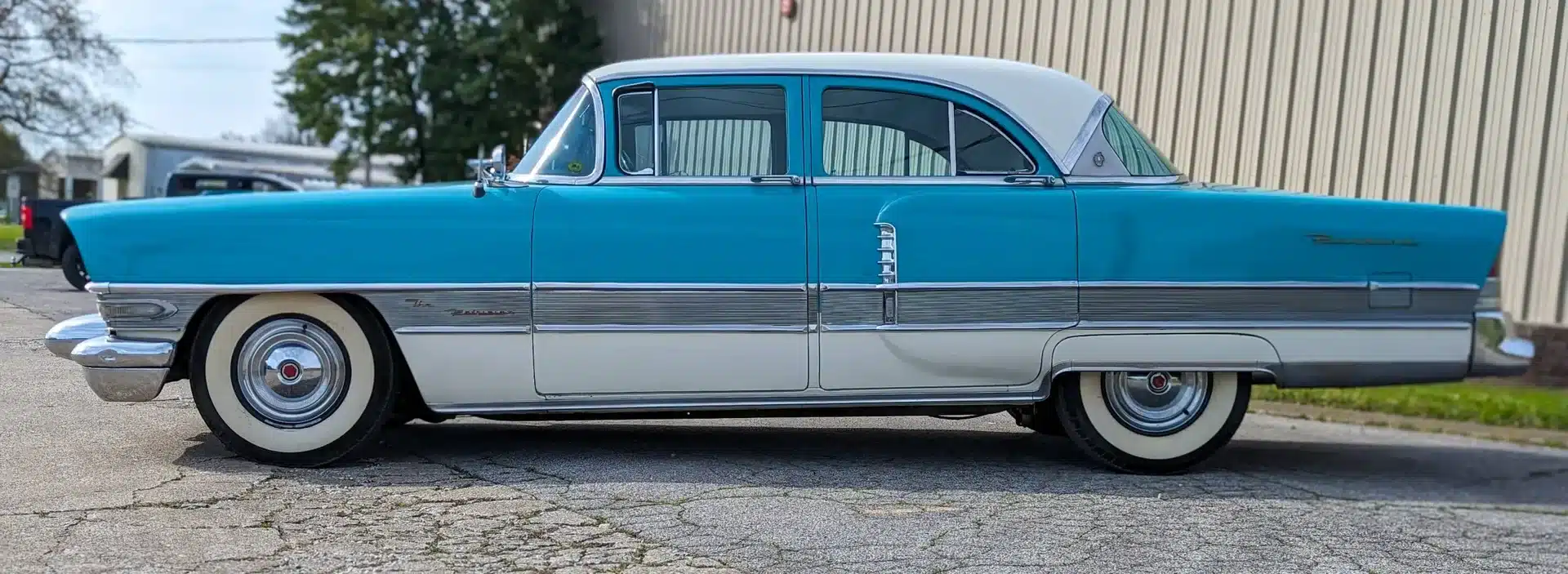 Seitenansicht eines türkis-weißen Packard Patrician von 1956, geparkt vor einer Halle.