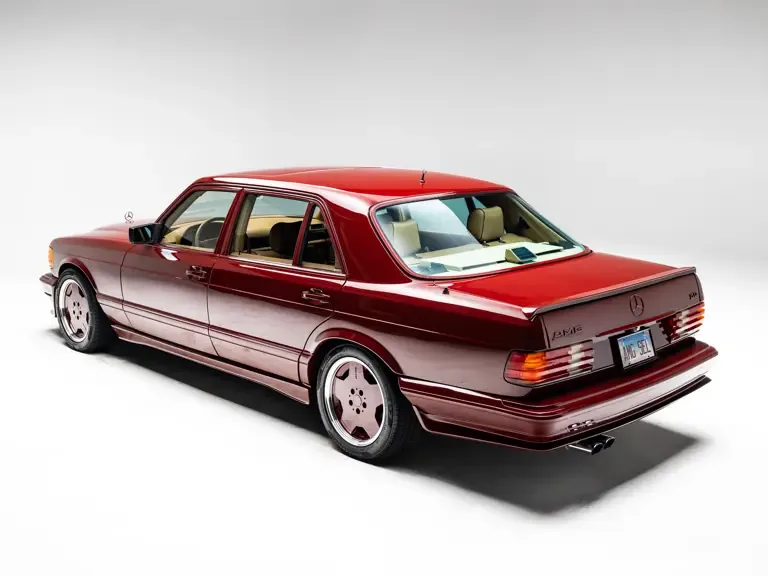 Heckansicht eines Mercedes-Benz 500 SEL 6.0 AMG W126 in Orientrot mit AMG-Paket und Aero-I-Felgen auf weißem Hintergrund.