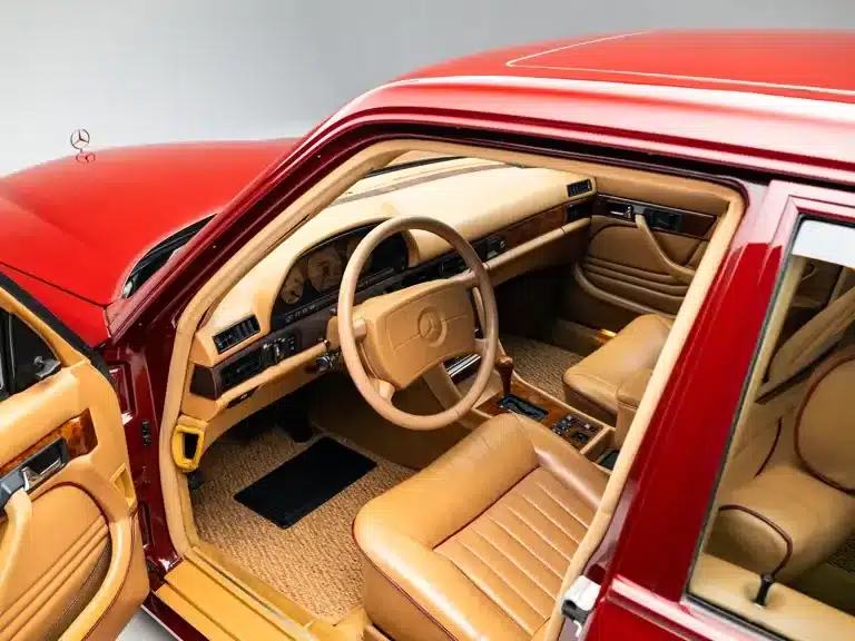 Der luxuriöse Innenraum eines Mercedes-Benz 500 SEL 6.0 AMG 'Red Baron' mit beigen Ledersitzen und klassischem Armaturenbrett, fotografiert durch die geöffnete Fahrertür.