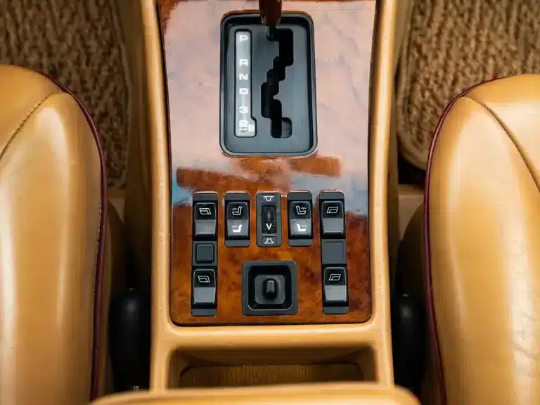 Nahaufnahme der Mittelkonsole mit Automatik-Wählhebel und elektrischen Bedienelementen im Mercedes-Benz 500 SEL 6.0 AMG, Baujahr 1983.