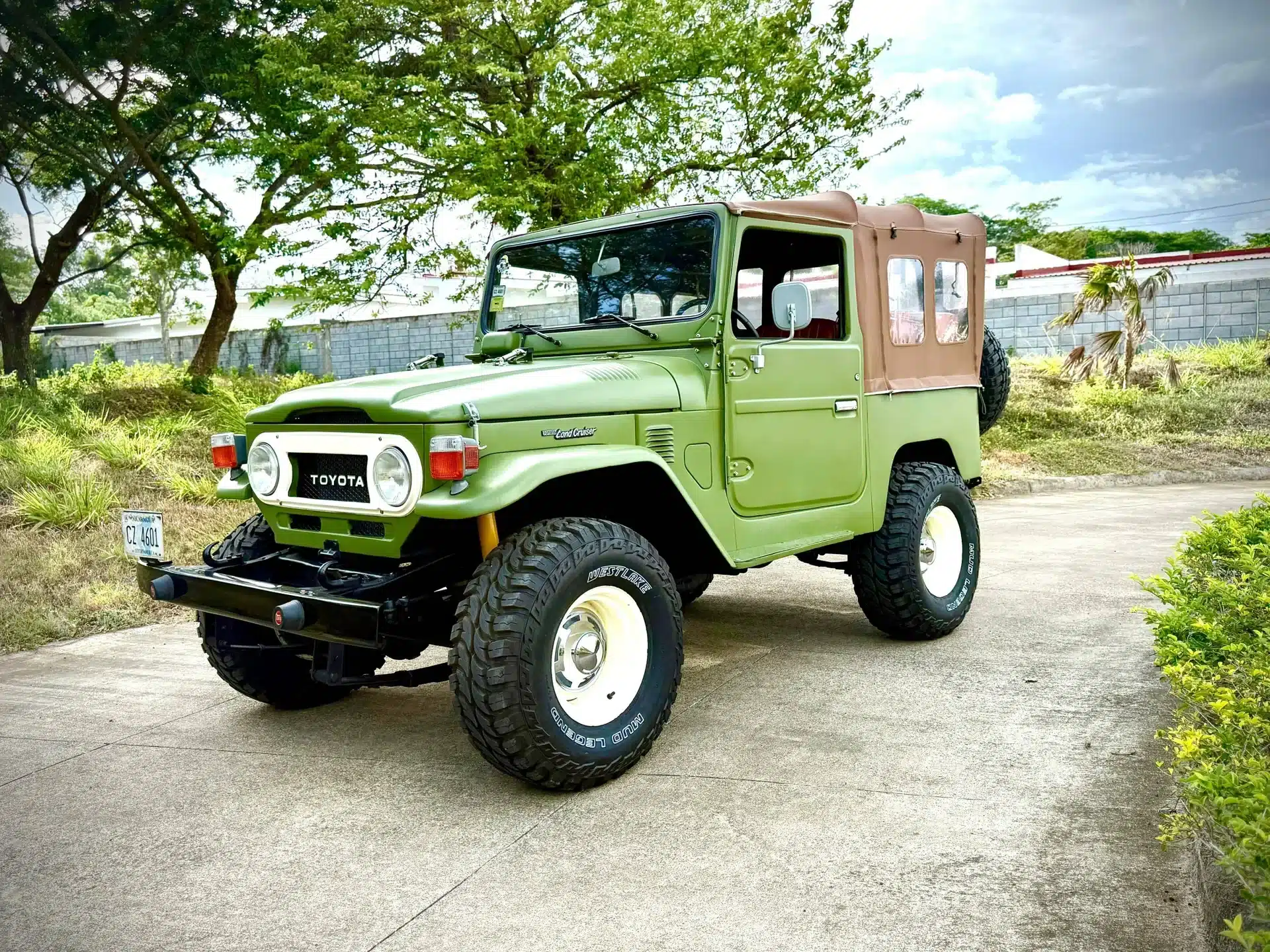 Grüner Toyota Land Cruiser FJ40 von 1978 mit Softtop, geparkt auf einem Weg unter Bäumen