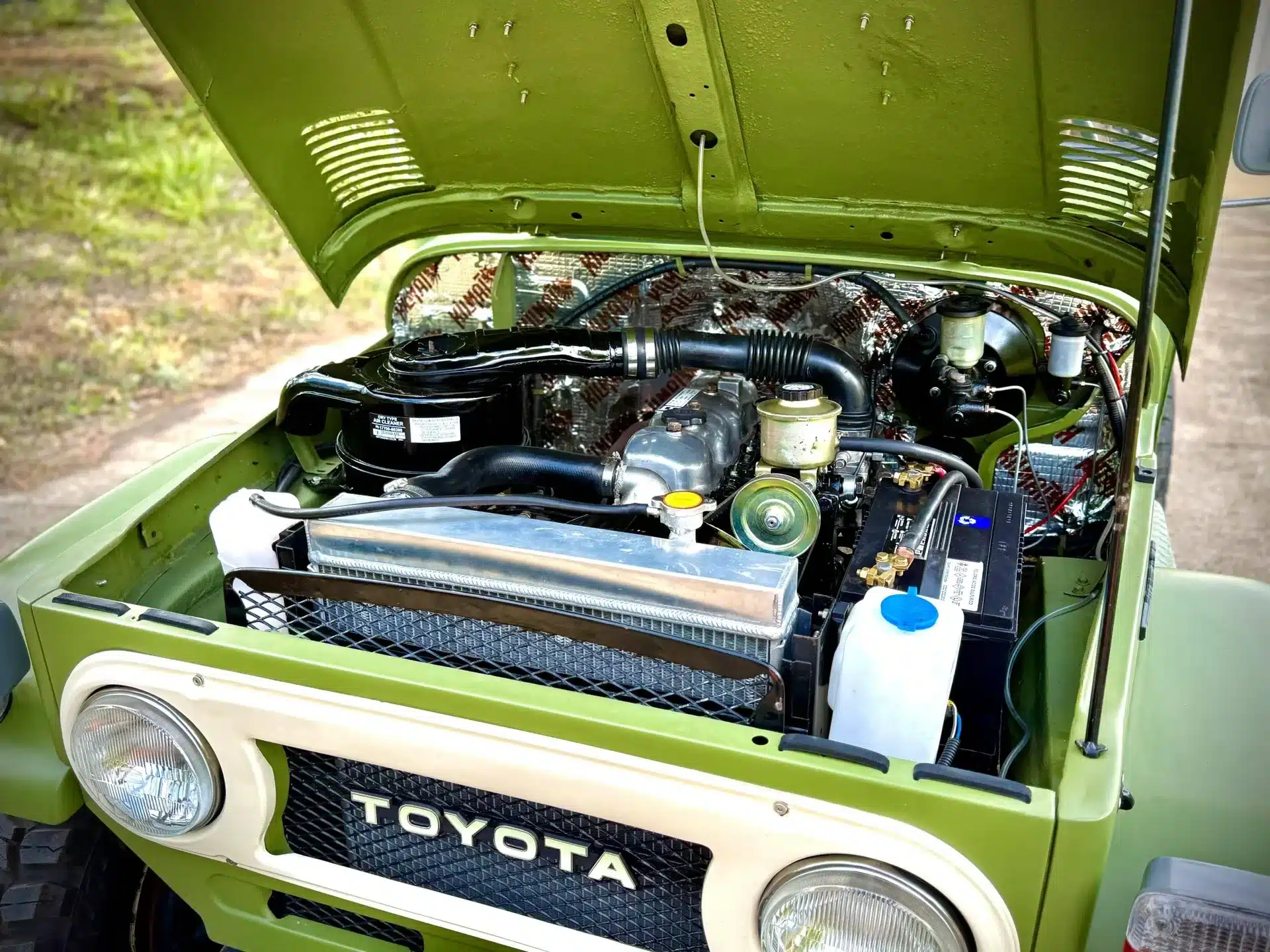Geöffnete Motorhaube eines Toyota Land Cruiser von 1978 mit sichtbarem Motorraum und Originaldetails.