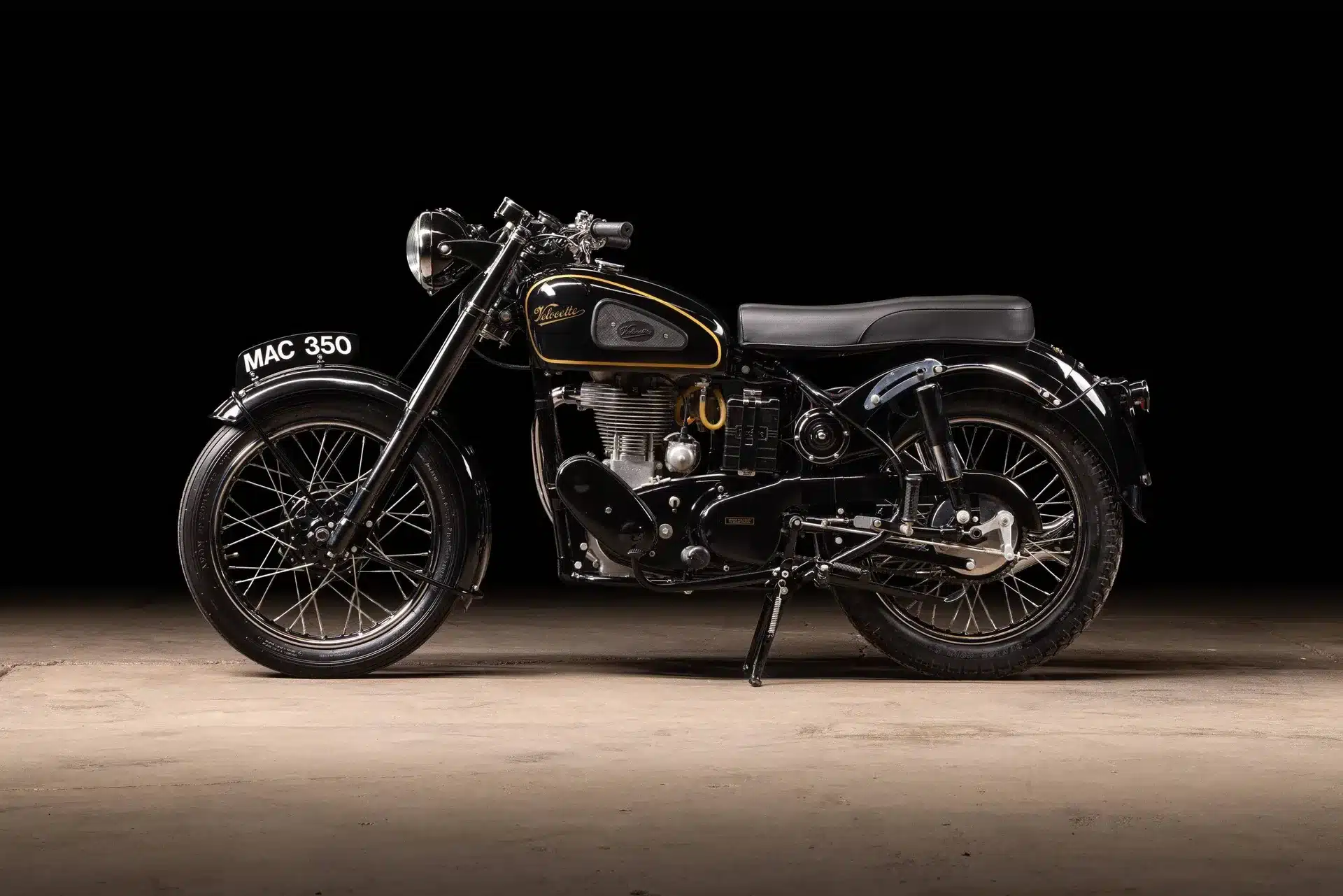 Seitenansicht einer restaurierten Velocette MAC 350 aus dem Jahr 1953 mit schwarzem Lack und goldenen Zierlinien vor dunklem Hintergrund
