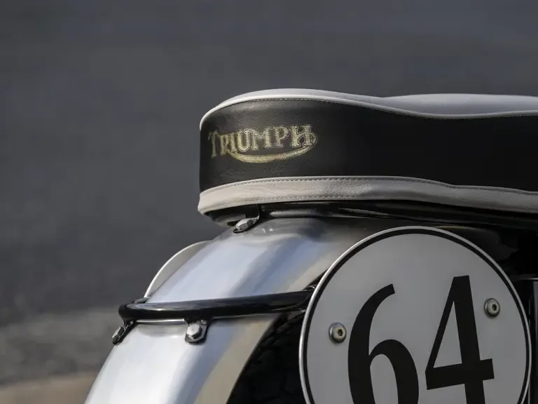 Nahaufnahme der Sitzbank mit Triumph-Logo und Startnummer 64 an einer restaurierten Triumph Bonneville TT Special.