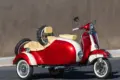 Restaurierte Piaggio Vespa 150 Super (1966) mit zweifarbig lackiertem Beiwagen, Weißwandreifen und beigen Einzelsätteln, stehend vor einer grauen Wand.
