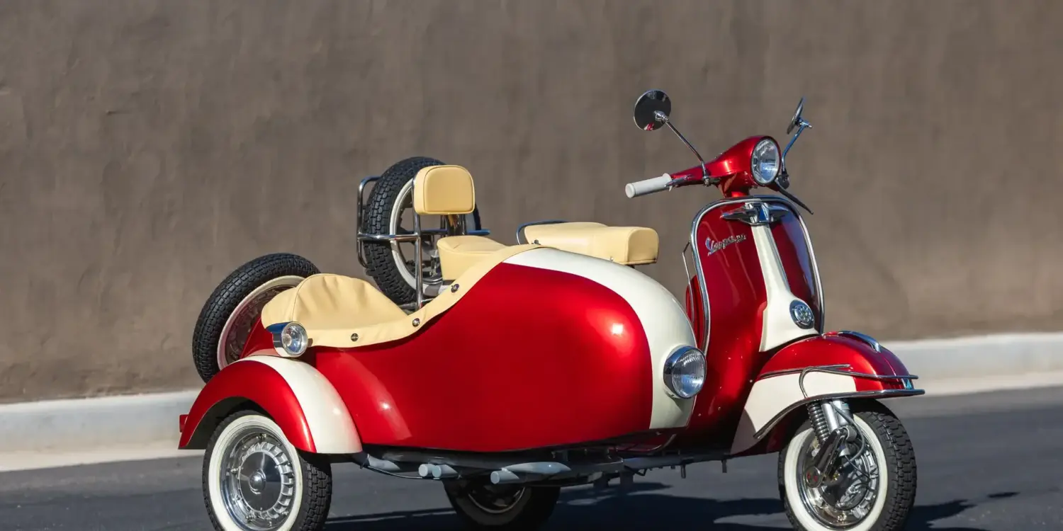 Restaurierte Piaggio Vespa 150 Super (1966) mit zweifarbig lackiertem Beiwagen, Weißwandreifen und beigen Einzelsätteln, stehend vor einer grauen Wand.