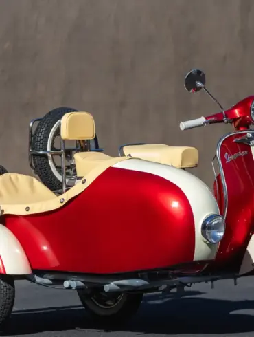 Restaurierte Piaggio Vespa 150 Super (1966) mit zweifarbig lackiertem Beiwagen, Weißwandreifen und beigen Einzelsätteln, stehend vor einer grauen Wand.