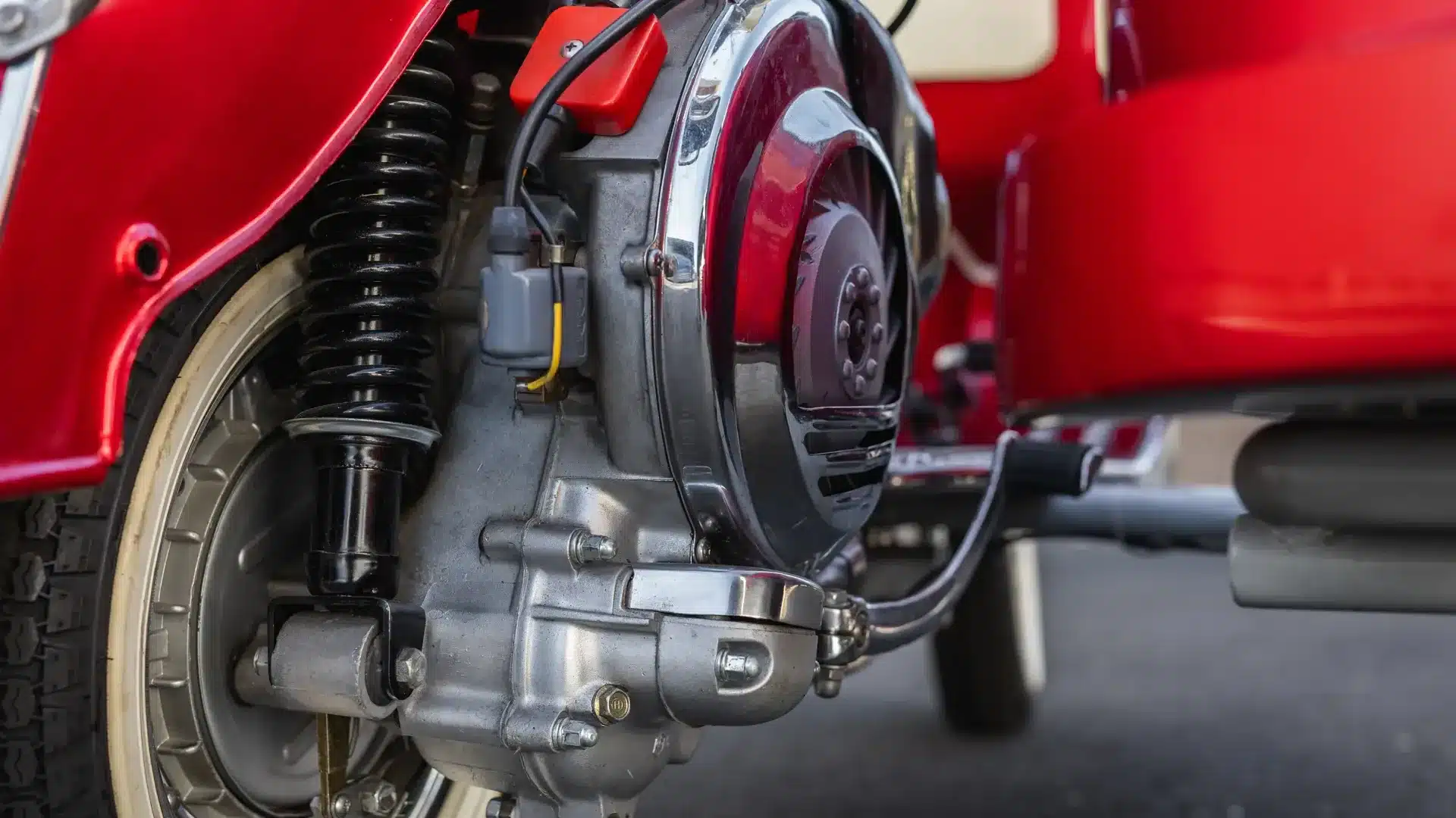 Nahaufnahme des Motors und Federbeins einer restaurierten Piaggio Vespa 150 Super von 1966 mit Beiwagen in Rot-Weiß.