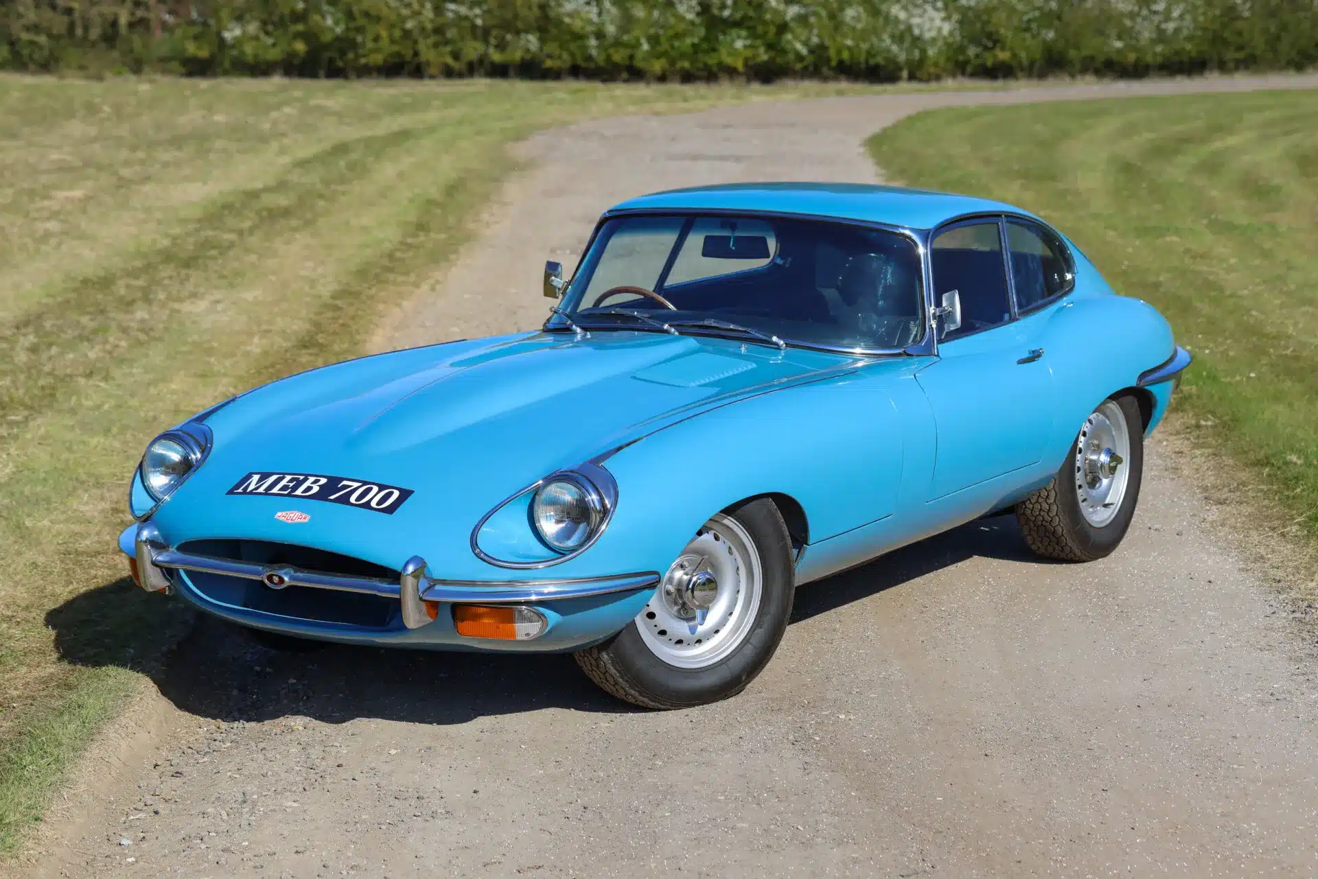Jaguar E-Type 4.2 Series 2 Coupé von 1969 in hellblauer Lackierung, frontal und seitlich fotografiert auf einer Landstraße.