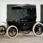 Duryea Four Wheel Phaeton von 1905 mit offener Karosserie und weißen Reifen vor Toren
