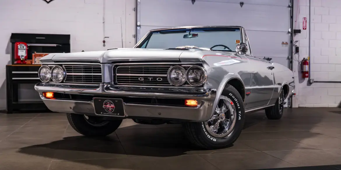 Silberner Pontiac GTO Cabrio aus dem Baujahr 1964 in einer Werkstatt, frontal fotografiert.