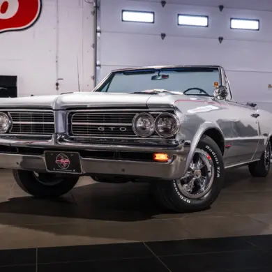Silberner Pontiac GTO Cabrio aus dem Baujahr 1964 in einer Werkstatt, frontal fotografiert.