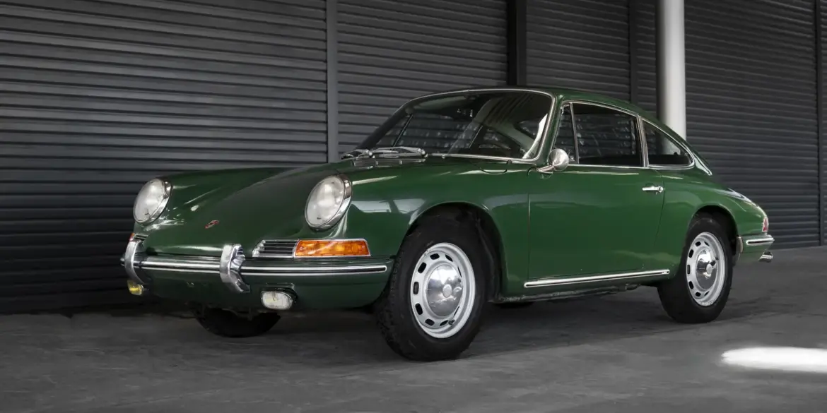 Ein grüner Porsche 911 Coupé aus dem Baujahr 1966 in unrestauriertem Originalzustand, seitlich in einer Halle fotografiert.