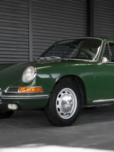 Ein grüner Porsche 911 Coupé aus dem Baujahr 1966 in unrestauriertem Originalzustand, seitlich in einer Halle fotografiert.