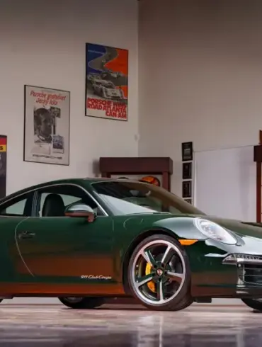 Porsche 911 Carrera S Club Coupé von 2013 in dunklem Grün, Seitenansicht in einer Garage vor Motorsportpostern.