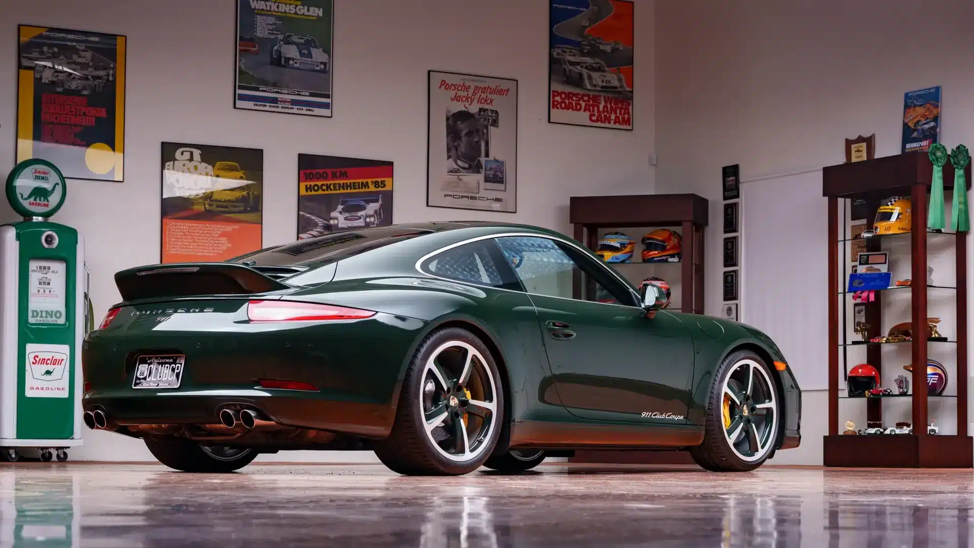 Porsche 911 Carrera S Club Coupé (2013) in Brewster Green von schräg hinten mit Ducktail, 20-Zoll-Rädern und Club-Coupé-Schriftzug, ausgestellt in einer mit Rennsport-Postern dekorierten Garage