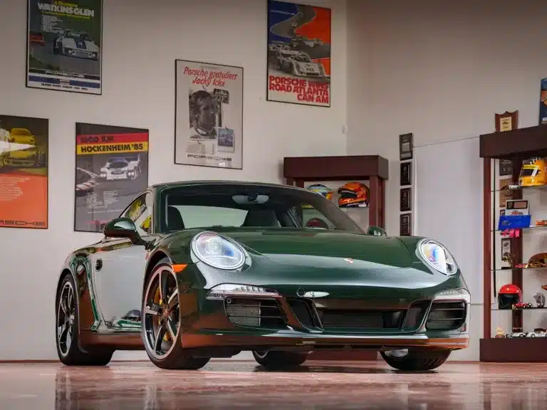 Porsche 911 Carrera S Club Coupé von 2013 in dunklem Grün in einer automobilen Ausstellung mit historischen Postern und Helmen.