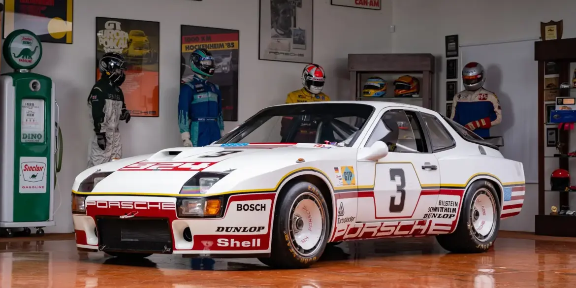 Porsche 924 GTP Le Mans 1980, weiß mit Startnummer 3, in einem Sammlerraum vor Rennanzügen und Motorsport-Postern