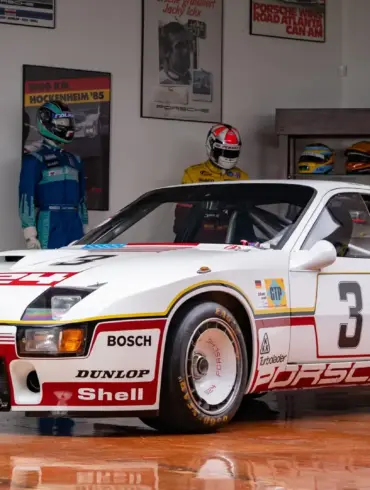 Porsche 924 GTP Le Mans 1980, weiß mit Startnummer 3, in einem Sammlerraum vor Rennanzügen und Motorsport-Postern
