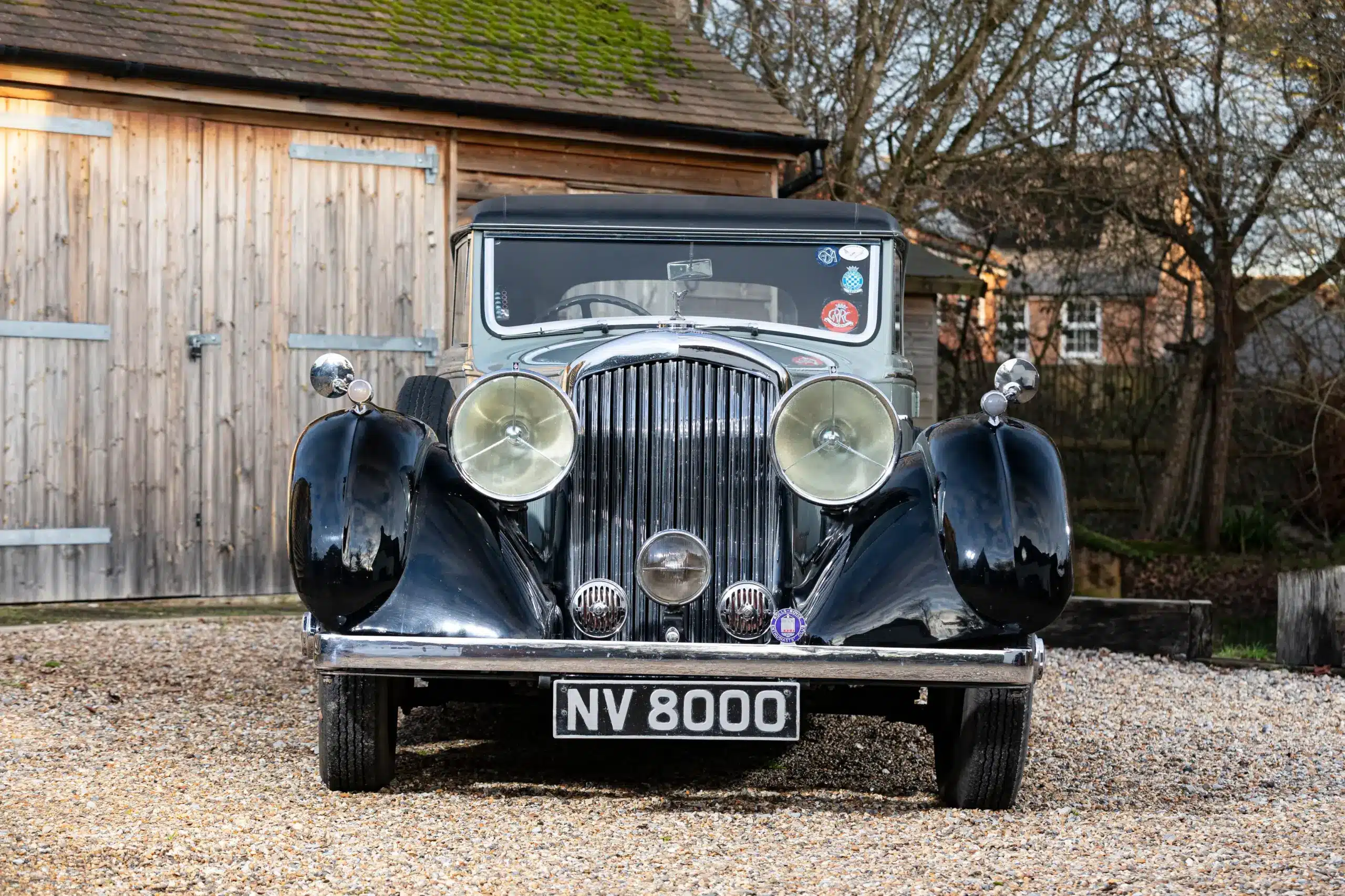 Frontalaufnahme eines Bentley 4 1/4 Litre Coupé von 1936, Oldtimer mit schwarzen Kotflügeln und runden Scheinwerfern, vor einer Holzgarage geparkt.