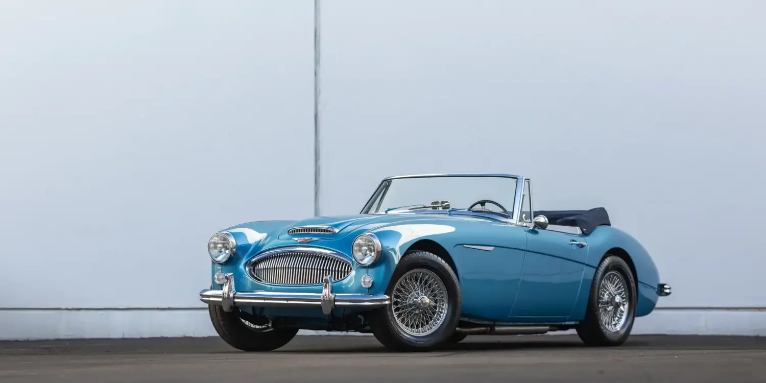 Austin-Healey 3000 Mk III BJ8 1965 in Blau, offen, vor heller Wand, schräg von vorn fotografiert.