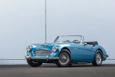 Austin-Healey 3000 Mk III BJ8 1965 in Blau, offen, vor heller Wand, schräg von vorn fotografiert.