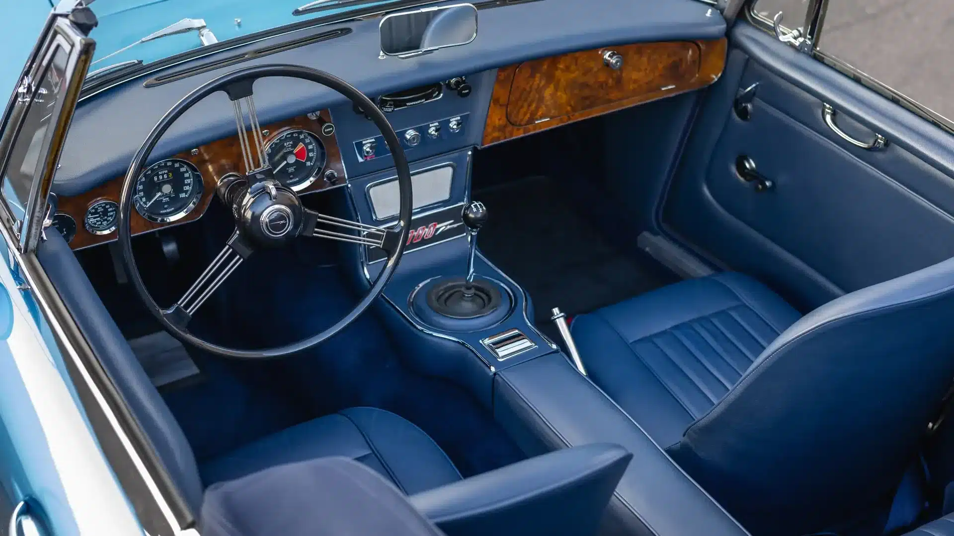 Innenraum des Austin-Healey 3000 Mk III BJ8 von 1965 mit Holzarmatur, blauer Lederausstattung und klassischem Lenkrad.