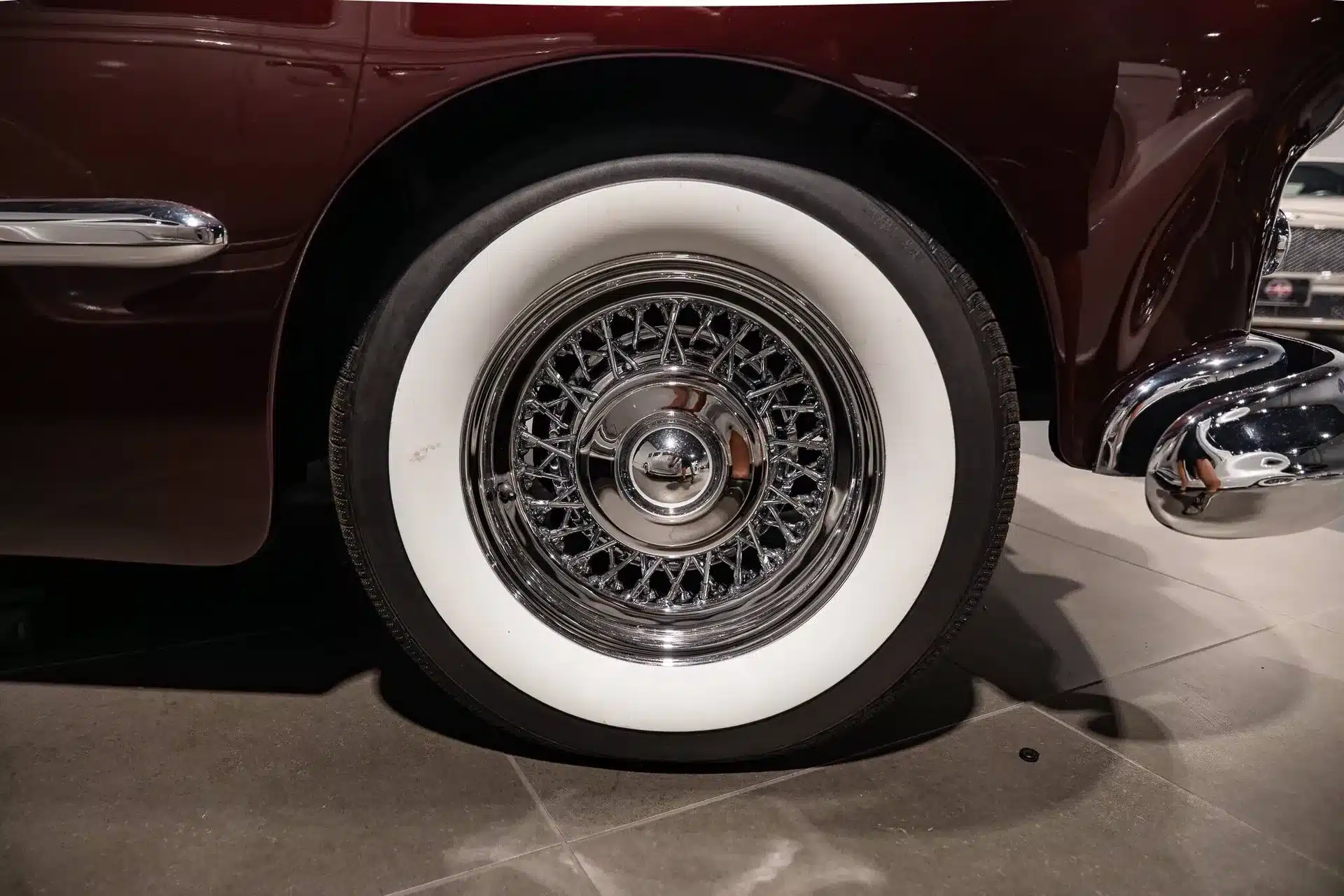 Nahaufnahme eines klassischen Weißwandreifens mit Drahtspeichen und Chromfelge an einem burgunderroten Oldtimer, vermutlich Oldsmobile 88 von 1948.