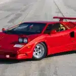 Roter Lamborghini Countach 25th Anniversary Edition, Baujahr 1989, mit geöffneten Scheinwerfern und markantem Heckflügel auf leerer Straße