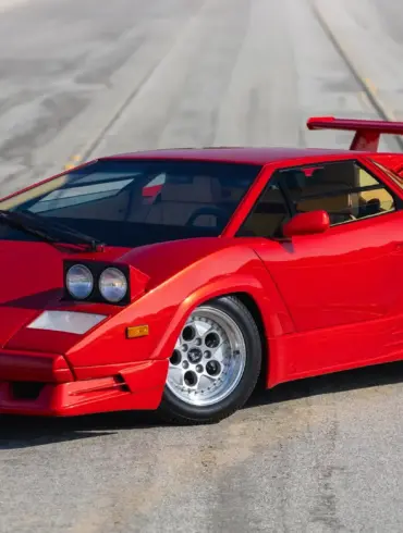 Roter Lamborghini Countach 25th Anniversary Edition, Baujahr 1989, mit geöffneten Scheinwerfern und markantem Heckflügel auf leerer Straße