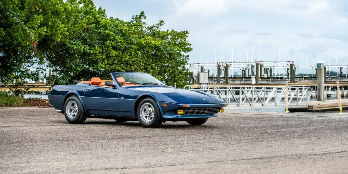 Blauer Ferrari 365 GTB/4 Daytona NART Spider by Michelotti, geparkt vor einer Marina, Seitenansicht mit orangem Lederinterieur.