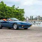 Blauer Ferrari 365 GTB/4 Daytona NART Spider by Michelotti, geparkt vor einer Marina, Seitenansicht mit orangem Lederinterieur.