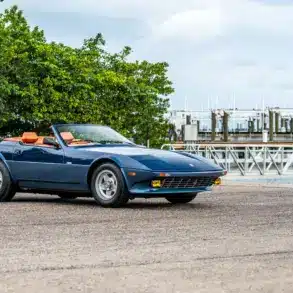 Blauer Ferrari 365 GTB/4 Daytona NART Spider by Michelotti, geparkt vor einer Marina, Seitenansicht mit orangem Lederinterieur.