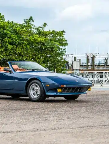 Blauer Ferrari 365 GTB/4 Daytona NART Spider by Michelotti, geparkt vor einer Marina, Seitenansicht mit orangem Lederinterieur.
