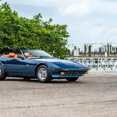 Blauer Ferrari 365 GTB/4 Daytona NART Spider by Michelotti, geparkt vor einer Marina, Seitenansicht mit orangem Lederinterieur.