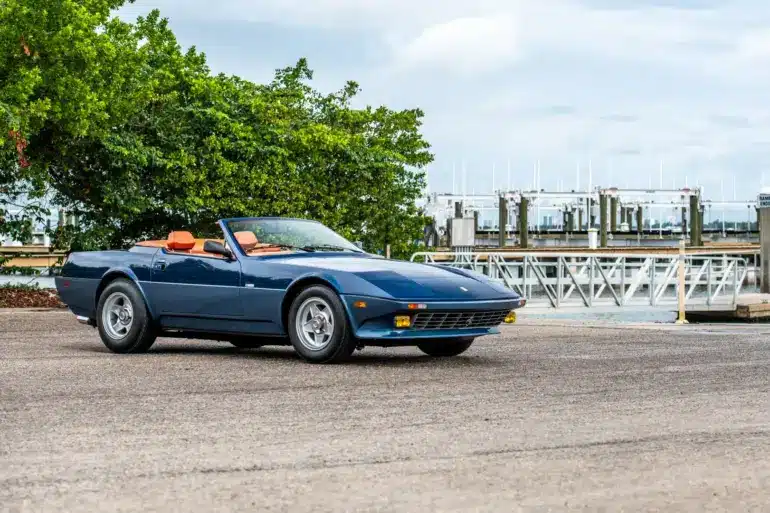 Blauer Ferrari 365 GTB/4 Daytona NART Spider by Michelotti, geparkt vor einer Marina, Seitenansicht mit orangem Lederinterieur.
