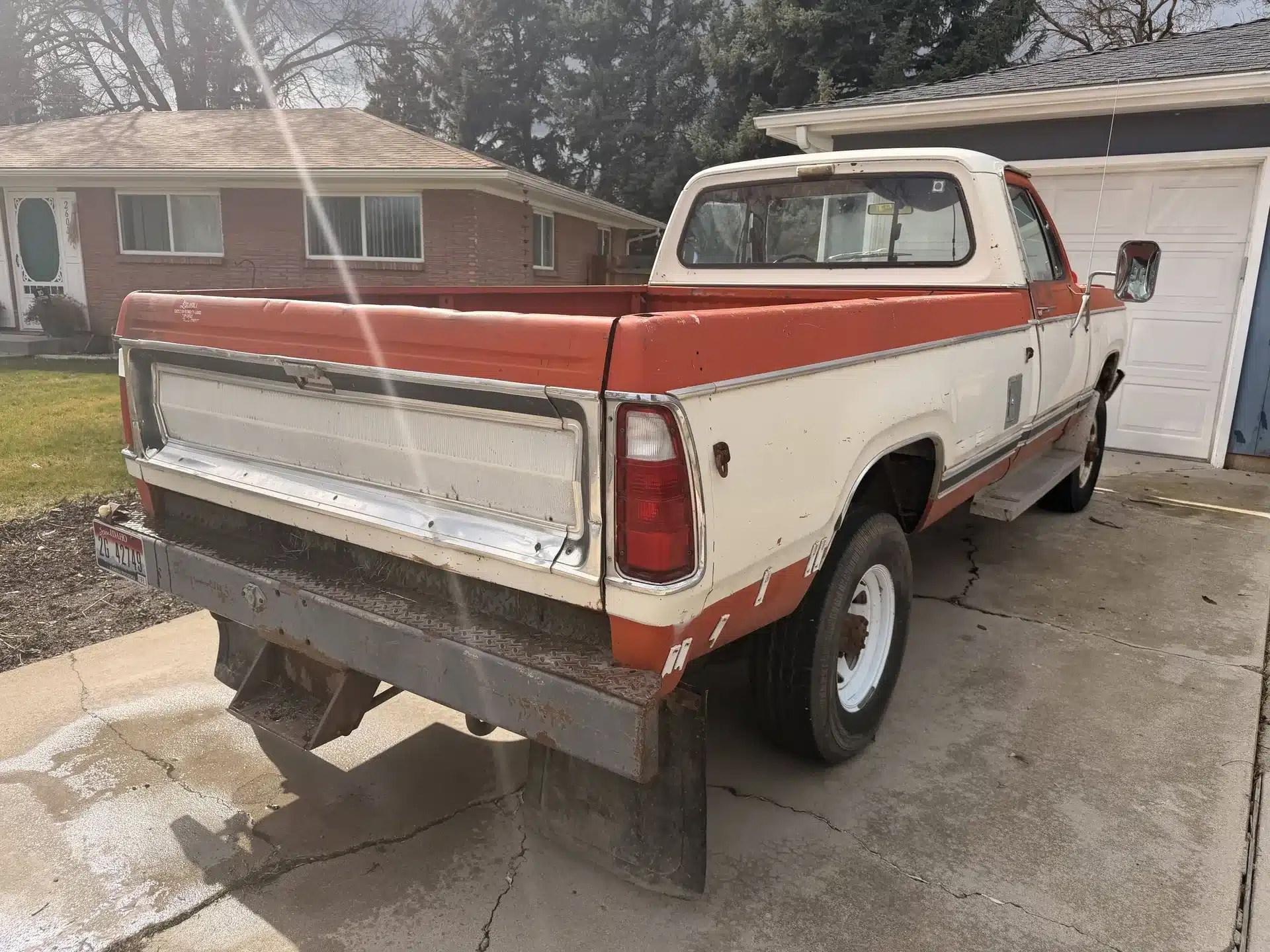 Dodge 200 Pickup von 1978 in weiß-orange auf einer Einfahrt, Rückansicht, Oldtimerzustand.