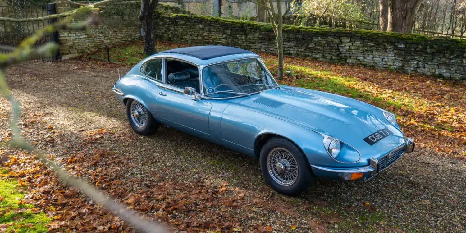 Jaguar E-Type Serie 1 4.2 Fixed Head Coupé 1965 in Opalescent Silver Blue, geparkt im Freien auf einem mit Laub bedeckten Kiesweg.