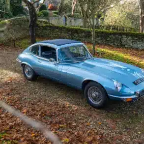 Jaguar E-Type Serie 1 4.2 Fixed Head Coupé 1965 in Opalescent Silver Blue, geparkt im Freien auf einem mit Laub bedeckten Kiesweg.
