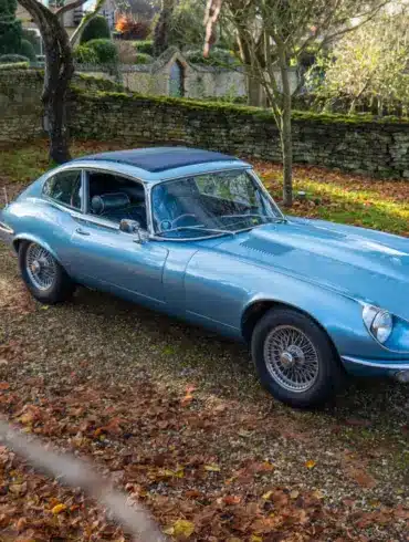 Jaguar E-Type Serie 1 4.2 Fixed Head Coupé 1965 in Opalescent Silver Blue, geparkt im Freien auf einem mit Laub bedeckten Kiesweg.